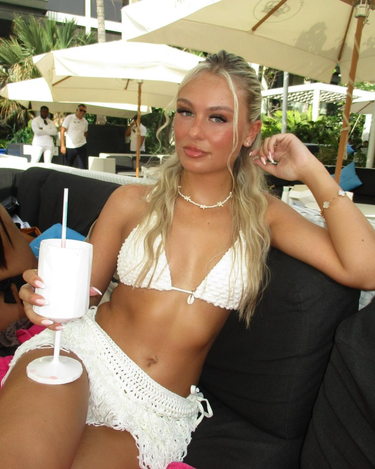 Woman in white bikini and concealment holding a drink.